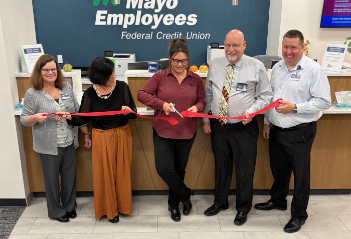 A group of five people stand in front of MEFCU sign, proudly cutting a ribbon to signify the opening of the newest office location
