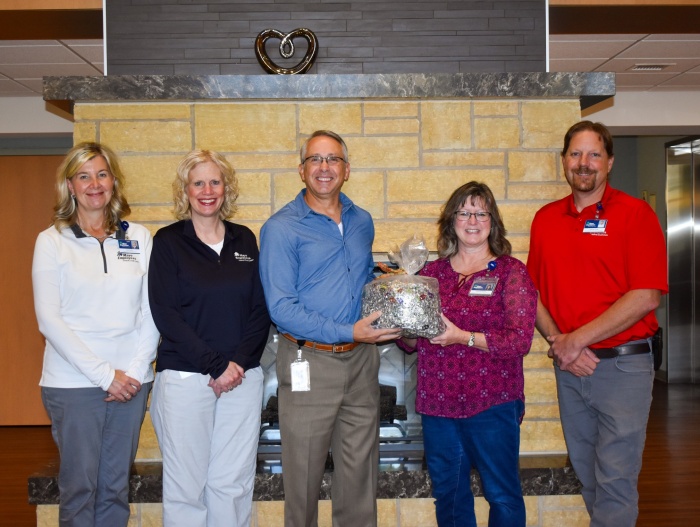 A group of five people stand in front of a fireplace, proudly presenting a bag of Pop-Tabs for the Ronald McDonald House.